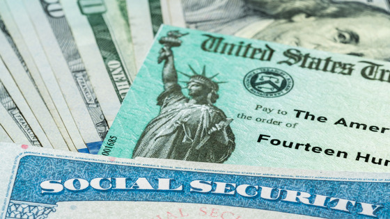 A social security card and U.S. Treasury check laying on top of a pile of $100 bills