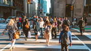 A crowd of people walking on the crosswalk of a busy street