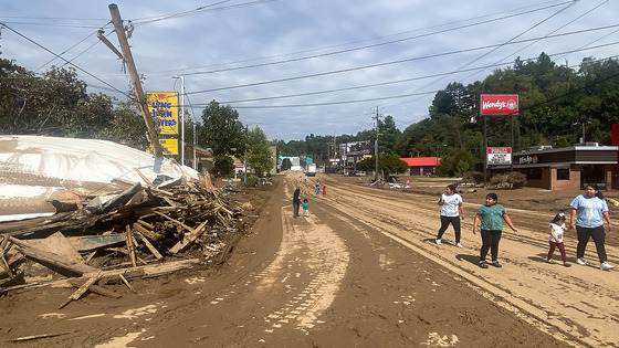 People walk down a muddy road in an area that has been devastated by a natural disaster.