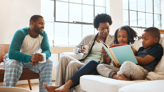 An African American family sitting in their living room reading a book