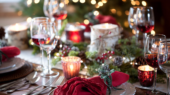 Holiday table setting featuring glasses, plates, silverware, and napkins.