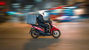  A person on a scooter drives with a delivery in tow. 