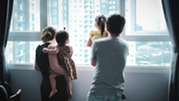 A family looks out the window of a high-rise apartment. 