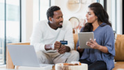 Two people sit on a couch and engage in a financial activity.