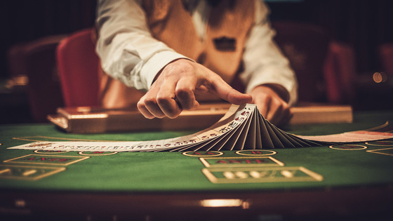 A casino dealer spreads a deck of cards across a green felt table.