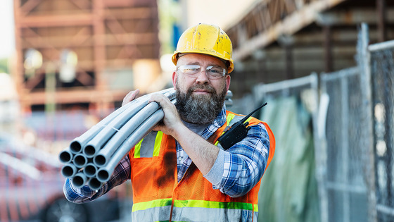 A construction worker carries pipes at a job site.