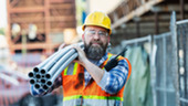 A construction worker carries pipes at a job site.