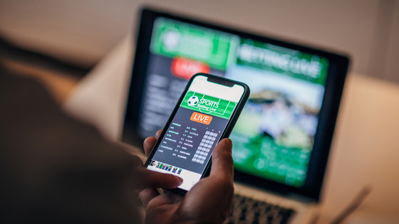 A person holds a smartphone displaying a live sports-betting app.