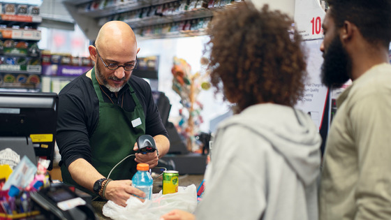 A cashier scans items for customers at a convenience store.
