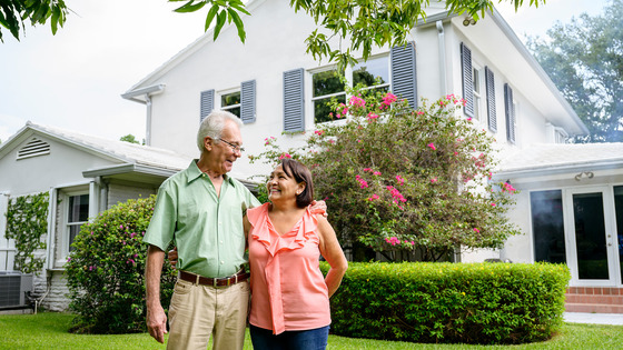 A couple stands in the front yard of their house.