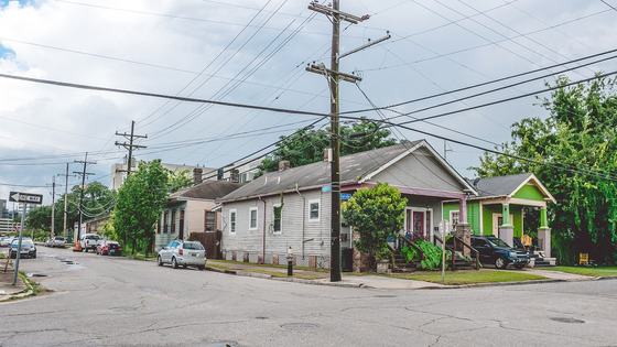 A residential street corner with houses, parked cars, and power lines. 