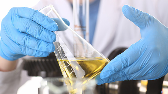 A person wearing blue gloves holds a laboratory flask containing a yellow liquid.  