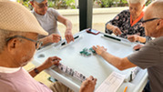 People sit at an outdoor table playing a tile game with domino-style pieces.