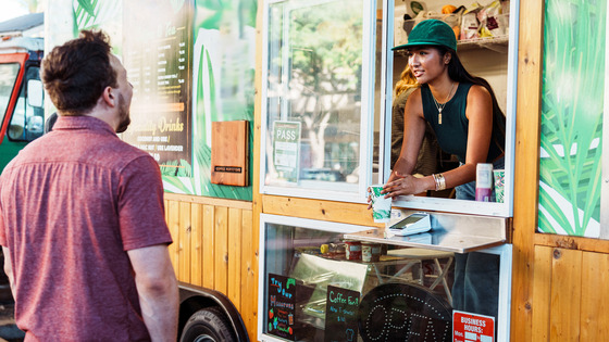 A person standing outside a food truck interacting with a worker at the service window