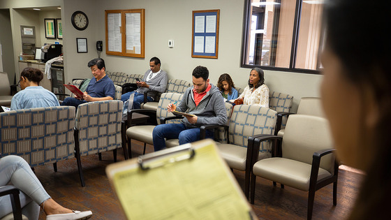 People seated in a waiting room filling out forms or reading.