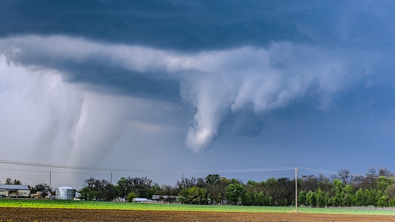 A dark storm cloud hangs over a field as a funnel begins to form.