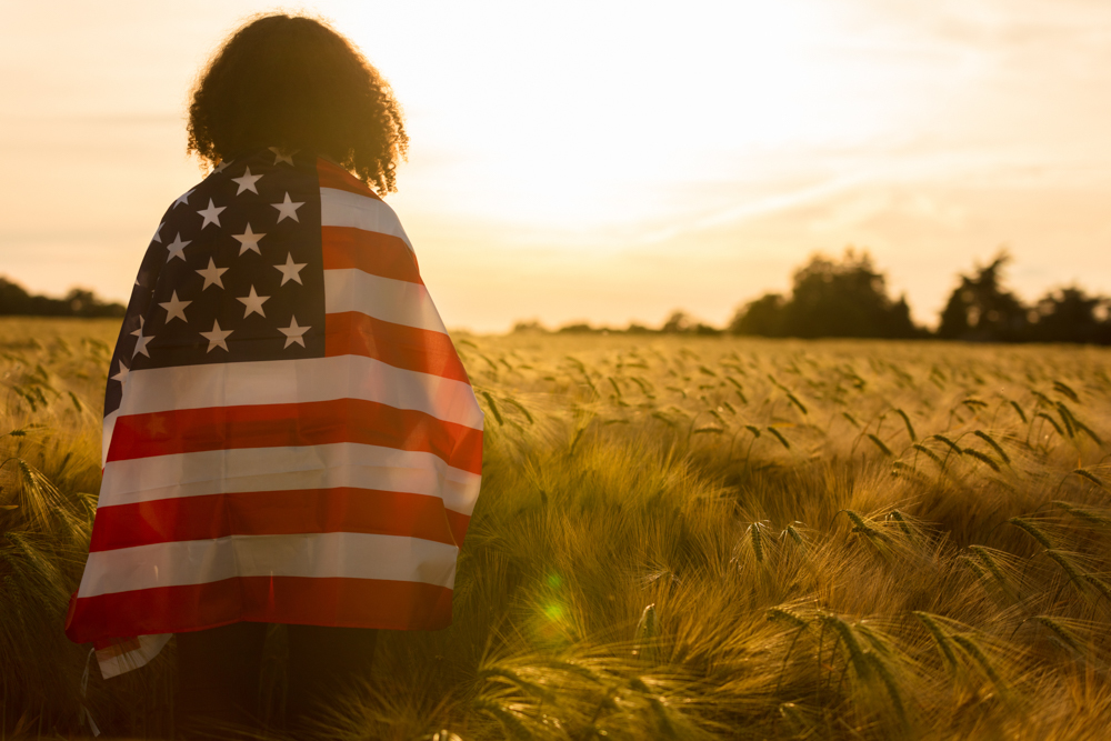 Young woman in a field of wheat and wrapped in U.S. flag