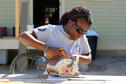 Corps Member using a handsaw on a construction site