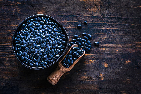 Black beans in a wooden bowl with a scoop of beans beside it. 