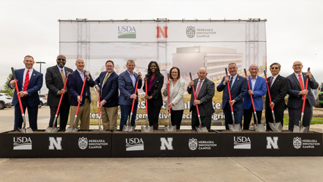 A group of 12 men and women in professional dress pose on stage with shovels