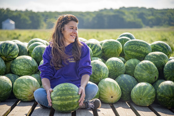 Image of a woman holding a watermelon standing near more watermelons