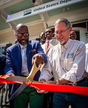 Chad Kacir and Ronald Guidry, Jr surrounded by attendees cut red ribbon on front porch of the New Orleans Urban Service Center