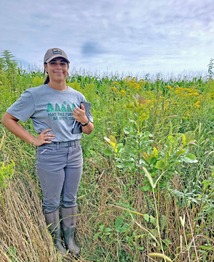 Earth Team Volunteer Isabelle Franks on a restored wetland mitigation site standing next to a swamp white oak sapling. 