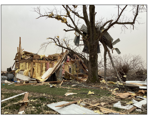 Photo of a house torn apart by storm activity on March 14, with debris hanging off a nearby tree and scattered in the foreground