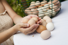 Basket of eggs on a counter and a woman holding 3 eggs