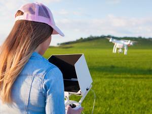 Woman operating drone over agricultural field, courtesy of Adobe Stock.
