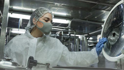Worker wearing mask and protective wear opening barrels while working at food factory. Photo courtesy of Adobe Stock.