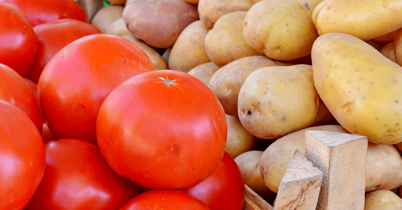 A stand of potatoes and tomatoes at a market, courtesy of Adobe Stock.