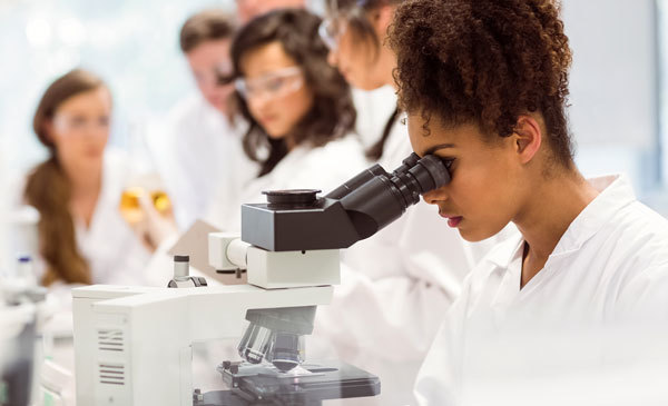 Funding opportunity for the RIIA and AGFEI programs. University student looking through a microscope, courtesy of Adobe Stock.