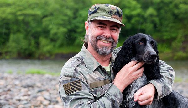 Smiling veteran with dog, image courtesy of Adobe Stock.