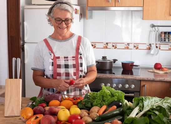 An older woman in her kitchen with fresh fruits and vegetables, courtesy of Adobe Stock.