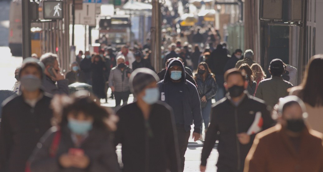 People in masks on a crowded urban street during the pandemic. Courtesy of Adobe Stock.