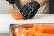 A gloved chef cuts salmon fillets. Courtesy of Adobe Stock.
