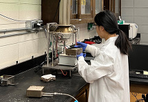 University of Idaho researcher Dr. Lili Cai performing fire test using a mass loss cone calorimeter under a hood. 