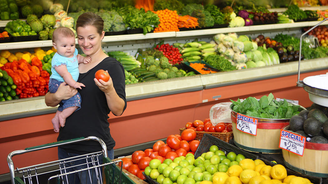 Mother with baby grocery shopping in produce section