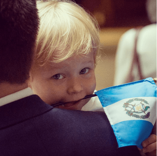 Erica Cox holds the flag of Guatemala (her future home), while her father Sean Cox is congratulated along with nine other employees of USDA's Foreign 