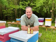 Jim Hartman surrounded by bee hives with bottle of honey in foreground