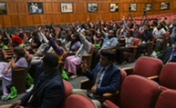 A group of about 90 Black students sitting in auditorium seating raising their hands.