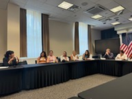 Dr. Lisa Ramirez (far left) talks to seven young adults seated at a conference table. 