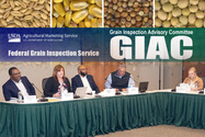 5 adults seated on a stage below a GIAC banner with pictures of different grains above.