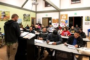 A classroom setting with a teacher standing at a podium speaking to seated students