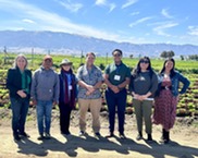 A group o adults stands in a row outside with mountains in the background