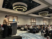 Lisa Ramirez addresses a crowded conference hall from podium