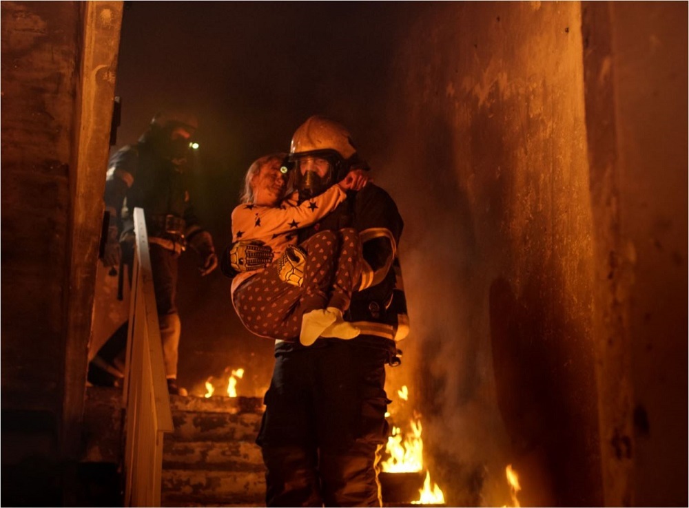 Firefighter caring a child out of a burning house.