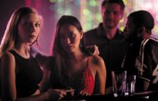 two men in the background looking at two women in the foreground of a nightclub scene. 
