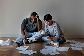 Couple sitting on floor reviewing documents strewn around them.